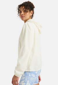 Lightweight white jacket with a hood, elastic cuffs, and a relaxed fit, paired with blue patterned shorts featuring floral designs.