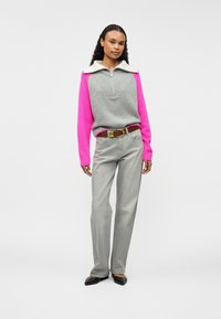 Pull en tricot gris avec des manches roses et un col blanc, associé à un jean droit gris clair et des chaussures noires à bout pointu.