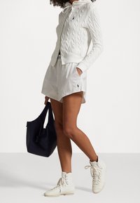 Vit kabelstickad zip-up hoodie, ljusa shorts med logotyp, marinblå totebag och vita hög-top sneakers. Fokusera på avslappnad, sportig estetik.