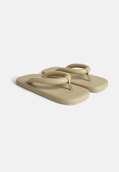 Beige flip-flops with a flat sole, featuring a contoured strap and a textured base. Made from a soft, flexible material.