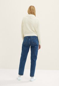 Maglione lavorato a maglia beige chiaro con colletto e motivo a trama aperta, abbinato a jeans in denim blu a vita alta e sneakers bianche.