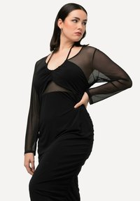 Schwarzes Kleid mit langen, durchsichtigen Mesh-Ärmeln, Raffung und taillierter Silhouette. Texturierter Stoff mit einem Halterneck-Design.