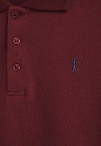 Vinröd pikétröja med tre knappar och liten broderad logga med en polo-spelare som håller en klubba på bröstet.