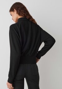 Pullover nero a maniche lunghe con colletto alto e bordo a coste, caratterizzato da una vestibilità ampia e una texture morbida, indossato sopra pantaloni scuri.