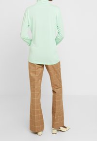 Mintfärgad långärmad polotröja med en slät textur, kombinerad med bruna rutiga utsvängda byxor med ett gult rutmönster och krämfärgade klackar.