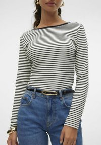 Langsleeve, gestreepte top in wit en zwart. De lichte stof heeft een boot halslijn. Gekocht met hoge taille blauwe denim jeans en een zwarte riem.