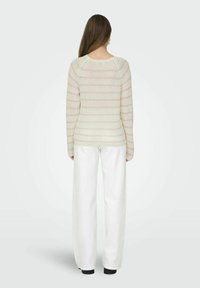 Brede gebreide pullover in crème met een pastel gestreept patroon, met een ronde halslijn en geribbelde manchetten, gecombineerd met witte wijde broekspijpen.