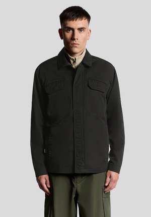 Sort jakke lavet af slidstærkt stof, med to brystlommer, en knappet front og lige snit. Båret over en beige top.