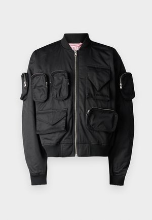 Black bomber jacket featuring multiple zippered pockets, ribbed cuffs, and collar. Smooth texture with a heart-shaped pocket detail.