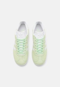 Zelené semišové tenisky s bílými akcenty, s kulatými tkaničkami, texturovanou špičkou a logem na jazyku.