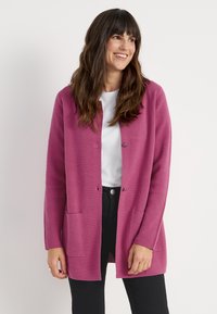 Långärmad, rosa cardigan gjord av texturerat tyg, med knäppning fram, två framfickor och en avslappnad passform.