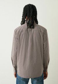 Koszula z długim rękawem w wąskie brązowe i kremowe pionowe paski, z zapięciem na guziki przy mankietach i standardowym kołnierzykiem. Wykonana z gładkiego materiału.