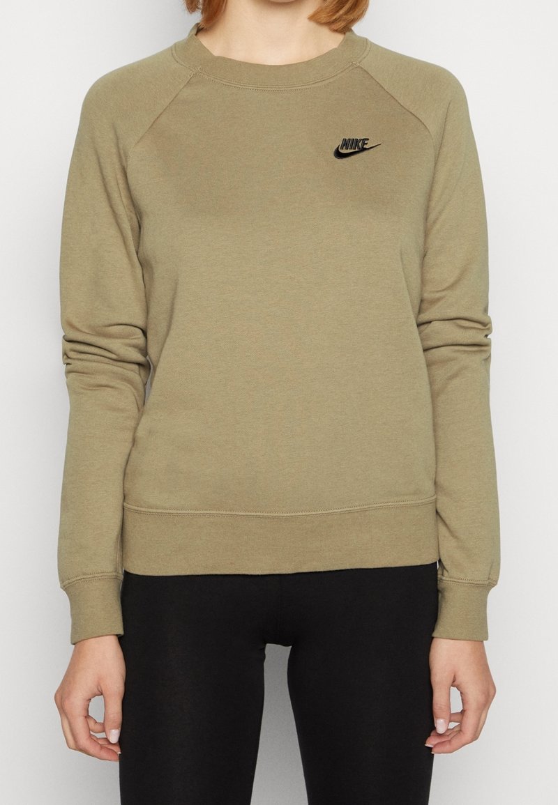 Woman wearing olive green Nike sweatshirt with black logo, paired with black leggings, standing against a plain white background.