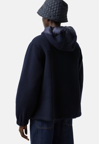 Granatowa polarowa kurtka z ocieplanym, pikowanym kapturem i elastycznymi mankietami, w zestawie z dopasowaną szaro-pikowaną kapeluszem typu bucket.