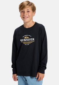 Čierne tričko s dlhým rukávom s okrúhlym logom Quiksilver v bielej a žltej farbe, vyrobené z bavlny, spárované so svetlomodrými džínami.