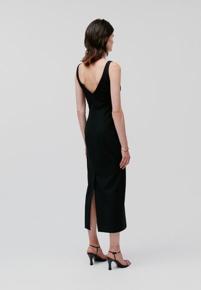 Black sleeveless dress with a V-back, fitted silhouette, and knee-length hem. Features a center back slit for ease of movement.