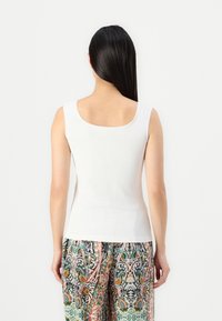 Top sin mangas blanco de canalé con un escote en la espalda. Combinado con pantalones coloridos y estampados que presentan diseños florales y paisley.