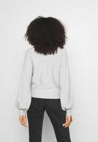 Pull en maille grise avec manches ballon, ourlet côtelé et finition texturée. Associé à un jean noir. Vue arrière uniquement.