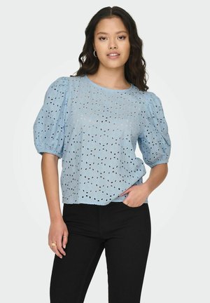 Lichtblauw, kortemouwen top met een relaxte pasvorm, voorzien van een laser-geknipt oogjes patroon en gathered puffmouwen, gecombineerd met zwarte jeans.
