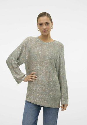 Pull à manches longues, ample en tricot argent métallisé avec un col rond et des poignets côtelés, associé à un jean bleu.