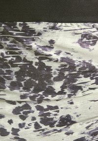 Le tissu de la robe sculptée présente une ceinture tissée noire. Le corps principal affiche un fond clair avec des motifs abstraits sombres et une subtile brillance.