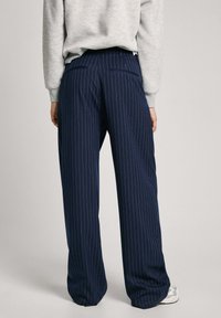 Pantalones a rayas navy de un tejido suave. Presentan un corte entallado, dos bolsillos traseros y una cintura de altura media.