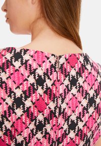 Enganliegendes Kleid mit einem floralen Muster in Pink, Weiß und Schwarz, ausgestattet mit einem dezenten Reißverschluss hinten und einem U-Boot-Ausschnitt.