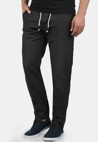 Pantalones de algodón negros con un ajuste relajado, que cuentan con cordones en color crema y bolsillos laterales. Combinados con zapatillas en color azul marino.