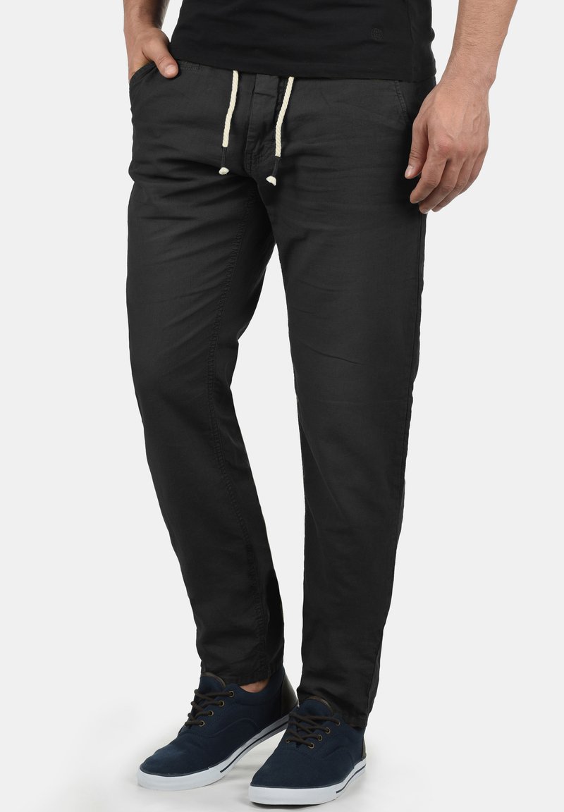 Pantalones de algodón negros con un ajuste relajado, que cuentan con cordones en color crema y bolsillos laterales. Combinados con zapatillas en color azul marino.