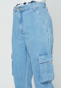 Jasnoniebieskie dżinsowe spodnie cargo o luźnym fasonie, z bocznymi kieszeniami, zapięciem na guzik i widocznymi detalami przeszyć.