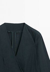 Black tailored blazer with wide lapels and a smooth, structured fabric visible on the shoulder and collar area.
