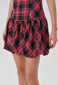 Gonna a bolla a quadretti rossi, neri e bianchi indossata da una persona, con lunghezza a metà coscia e dettagli di orlo arricciato.