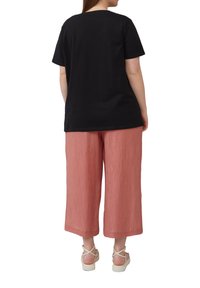 Zwarte t-shirt met korte mouwen gecombineerd met lichtroze wijde broek met een geribbelde textuur en beige sandaaltjes met banden.