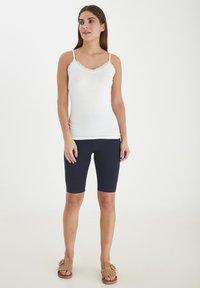 Camiseta de tirantes blanca con acentos de encaje, combinada con leggings navy de medio muslo y sandalias de tiras de mimbre color tostado. Diseño sencillo y ajustado.