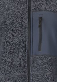 Mørkegrå fleecetrøje med frontlynlås og en brystlomme med lynlås, lavet af en glat stofpanel.