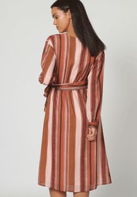 Vestido de manga larga con rayas verticales en marrón, rosa y rojo. El material parece ligero, con un cinturón en la cintura y un corte holgado.