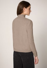 Beiger Rollkragenpullover aus weichem Stoff, mit gerippten Bündchen und Saum, kombiniert mit dunkelgrauer Hose.