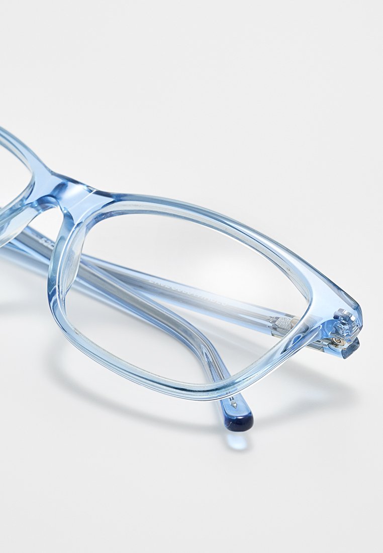 Gafas de vista transparentes en color azul con un marco rectangular. El diseño presenta bordes suaves y patillas ligeras con acentos de metal.