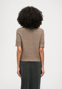 Brown short-sleeve sweater in soft, textured material with a fitted design, lower ribbed hem, and seamless shoulders, worn with a dark skirt.