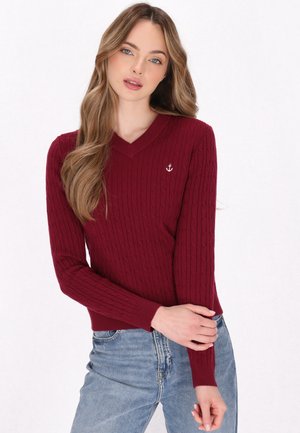 Bordeauxfarbener Strickpullover mit V-Ausschnitt, ausgestattet mit einem Zopfmuster und einem kleinen weißen Anker-Emblem auf der Brust. Enganliegende Passform mit langen Ärmeln.