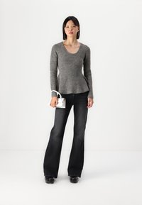 Grå tettstrikket genser med lange ermer, rund hals og utsvingt nederkant, kombinert med mørke utsvingte jeans og en liten hvit håndveske.