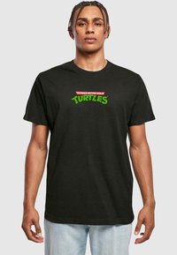 Black cotton t-shirt featuring a colorful "Teenage Mutant Ninja Turtles" logo in red and green, short sleeves, and a relaxed fit.