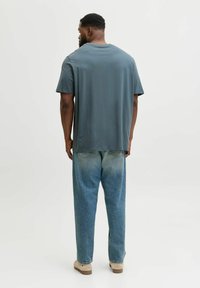 T-shirt grigio scuro con vestibilità comoda, abbinata a jeans in denim blu chiaro con aree sbiadite e tasche posteriori classiche.