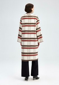 Lang, stribet uldfrakke i creme med brune og røde striber, med krave og brede ærmer, båret over sorte, flagrende bukser.