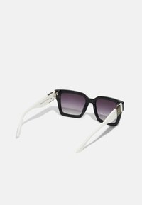 Lunettes de soleil noires en forme de carré avec des verres dégradés, branches blanches, accents en métal et détails de logo sur le côté. Monture en plastique durable.