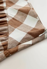 Tissu à carreaux marron et blanc avec bord froncé et tirette blanche sur une surface claire.