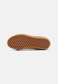 Bunnsikt av en sneaker med en gummigummi yttersåle som har et teksturert, diamantmønster i brun farge.