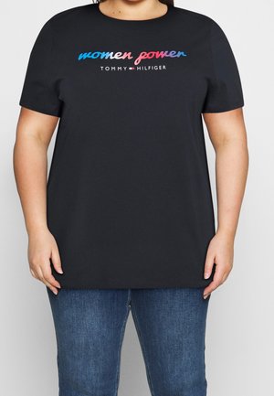 Sort T-shirt med "women power" i blåt og pink skrift og "Tommy Hilfiger" logo båret af en person i blå jeans.
