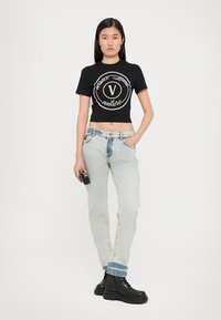 Juodas trumpas marškinėliai su kreminiu logotipu, šviesiai mėlyni džinsai su išblukusia apdaila ir juodi bateliai su raišteliais. Modelis laiko mažą juodą rankinę.