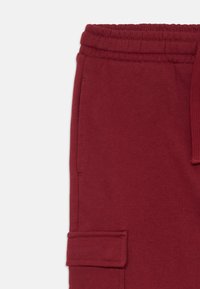 Burgunderfargede sweatpants med strukturert stoff, elastisk midjebånd og sidelommer. Designet inkluderer forsterkede sømmer og kontrasterende søm.